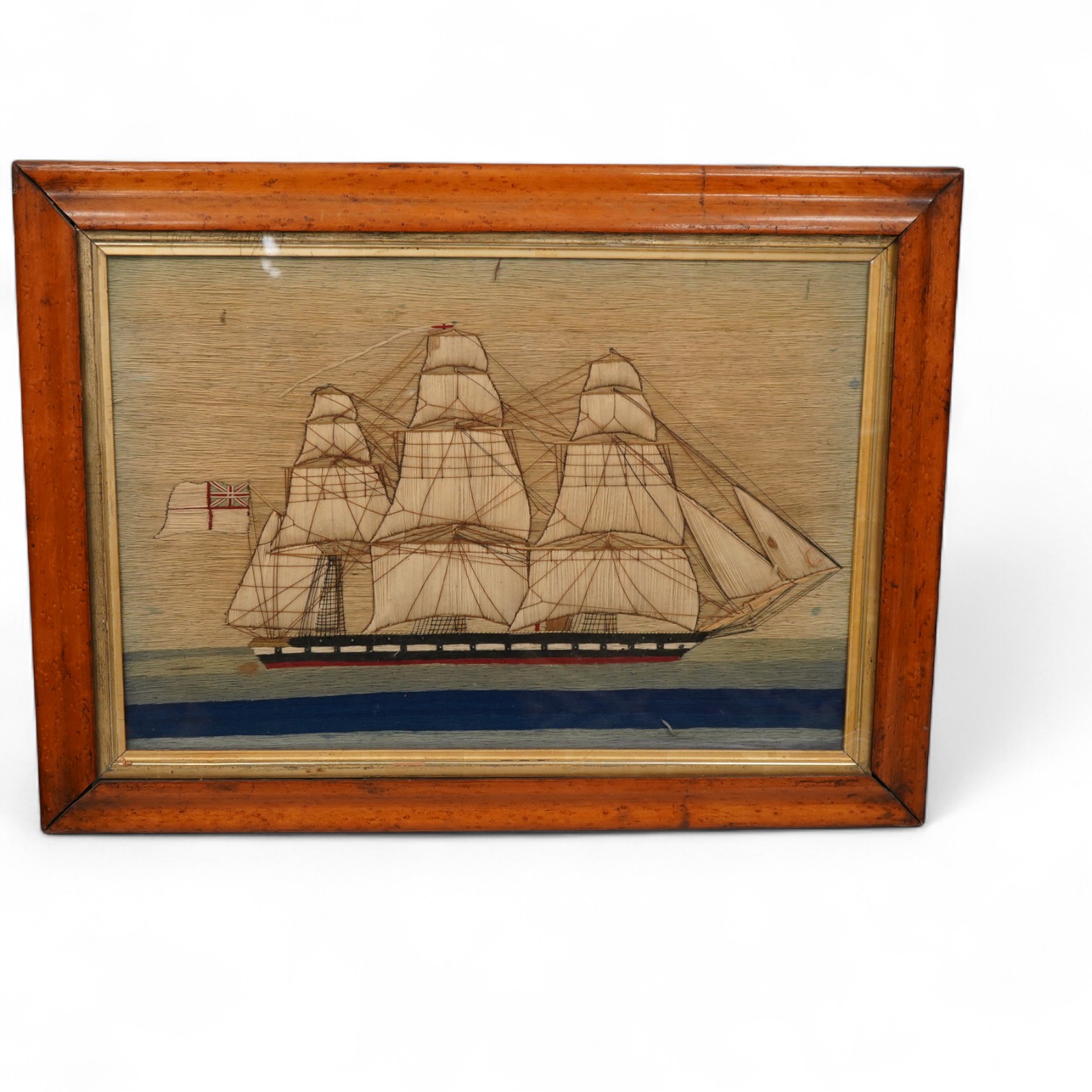 A maple framed 19th century ‘woolie’ folk art, wool work embroidery of a fully rigged sailing ship. Embroidered by a sailor using wading, creating raised stump work sails, using long straight stem stitches both verticall